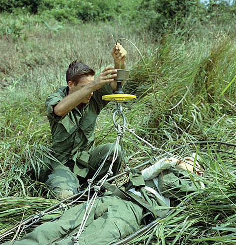 PFC James L. Morrison, a medic with the 45th Med. Co., straps a wounded man into a Stokes Rigid Litter to be hoisted into a UH-1D helicopter, Long Binh, September 1967